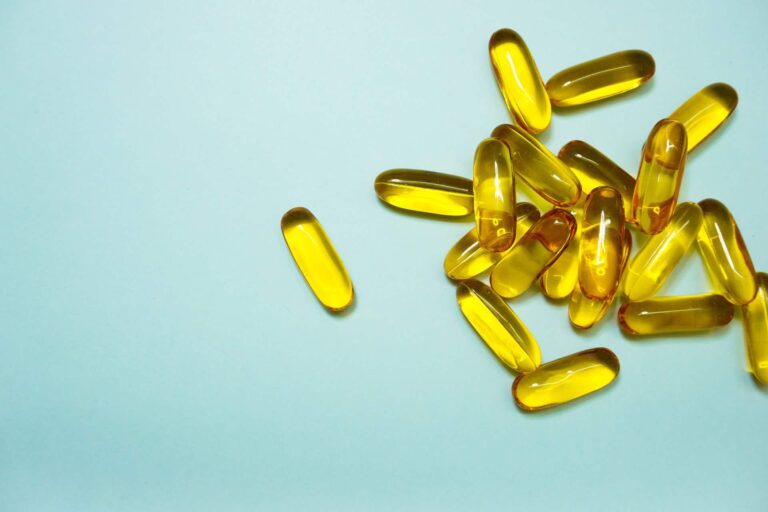 Omega-3 fish oil capsules. Yellow gel pills for healthy diet on blue background.