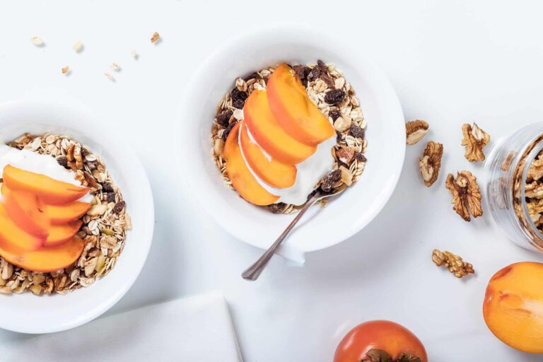 Healthy breakfast bowl: granola, yogurt, sliced persimmon, and walnuts. Nutritious morning meal.