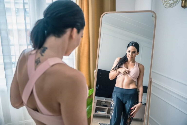 Fit woman checks her abs in mirror. Body transformation, healthy lifestyle.