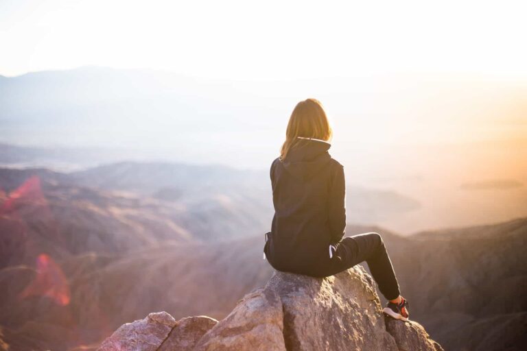 Woman sits on a rock, enjoying mountain view at sunset. Hiking and outdoor adventure.
